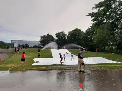 Kids sliding down a tarp water slide on a hill