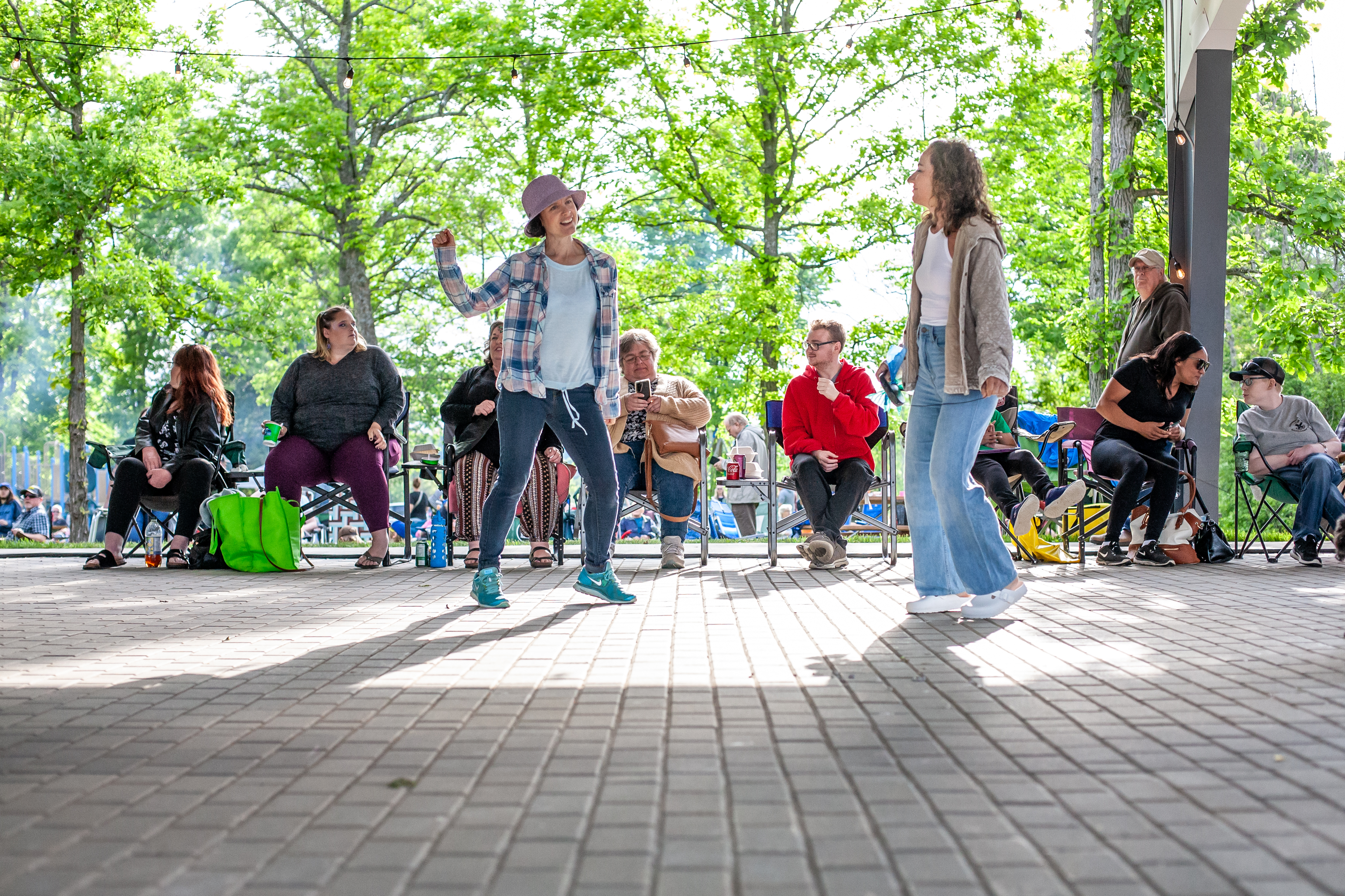 Two women dancing in the sun in front of people in lawn chairs.