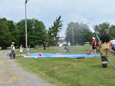A fire fighter holding a hose up spraying water on tarp for kids